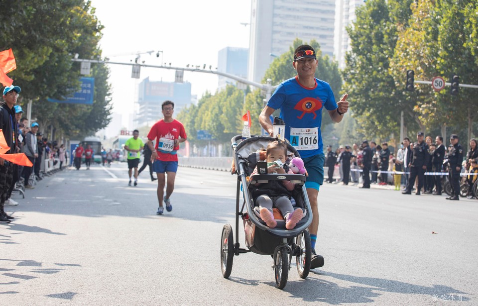 10月21日，一名选手手推婴儿车参加全程马拉松比赛。